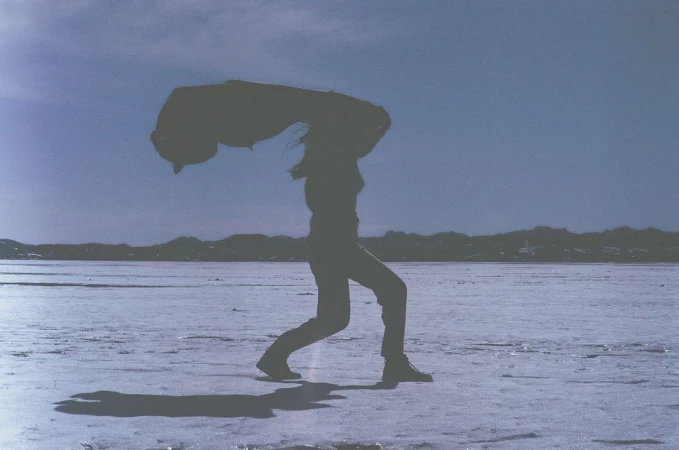 Silhouette of a person standing outdoors on a flat expanse holding a jacket overhead against a pale sky