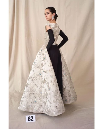 Woman in elegant gown with floral design and black arm gloves posing in a studio, beauty shot with neutral backdrop.