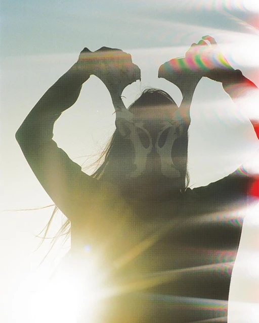 Silhouette of person holding antlers against a bright sky, creating a mystical and surreal effect with sun flare and lens refraction.