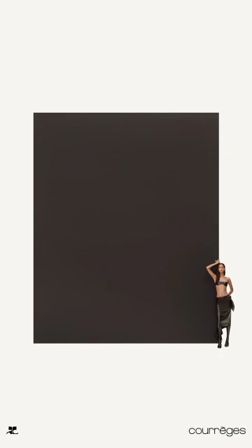Woman in a black two-piece outfit poses next to a large black square, minimalist fashion shot, against a cream-colored background.