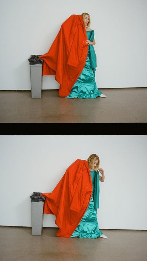 Woman in teal gown next to trash can covered in red fabric in studio, creating a surreal fashion shot with artistic composition.