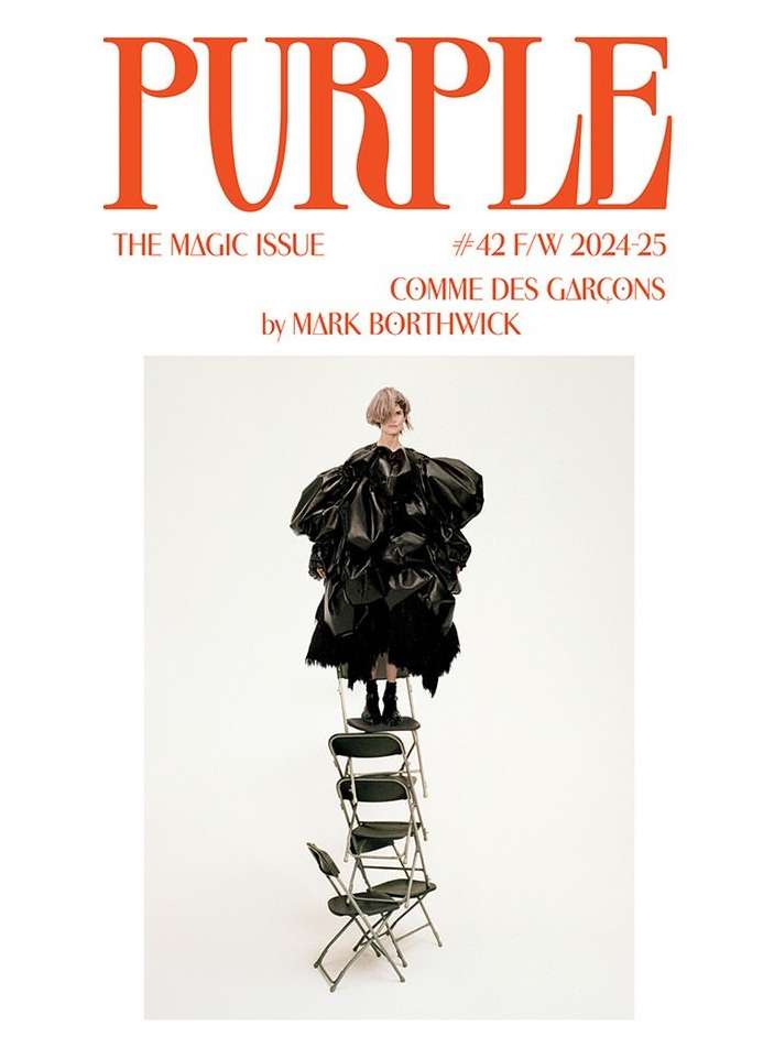 Fashion magazine cover featuring a model in a large black dress standing on a tower of folding chairs, against a white background.