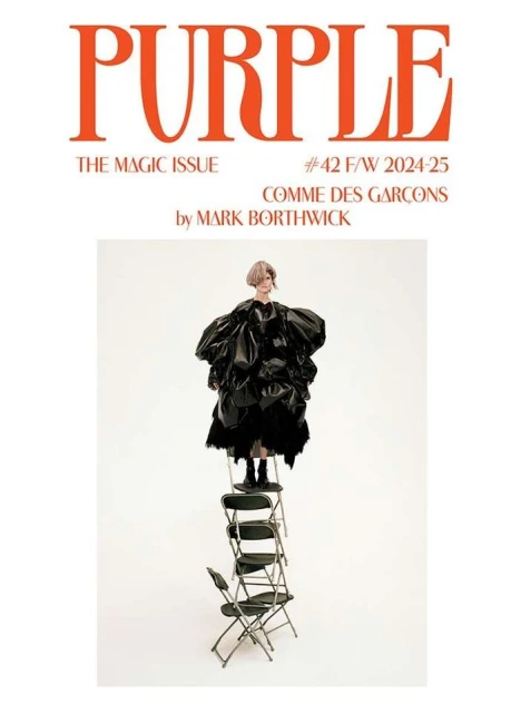 Fashion magazine cover featuring a model in a large black dress standing on a tower of folding chairs, against a white background.