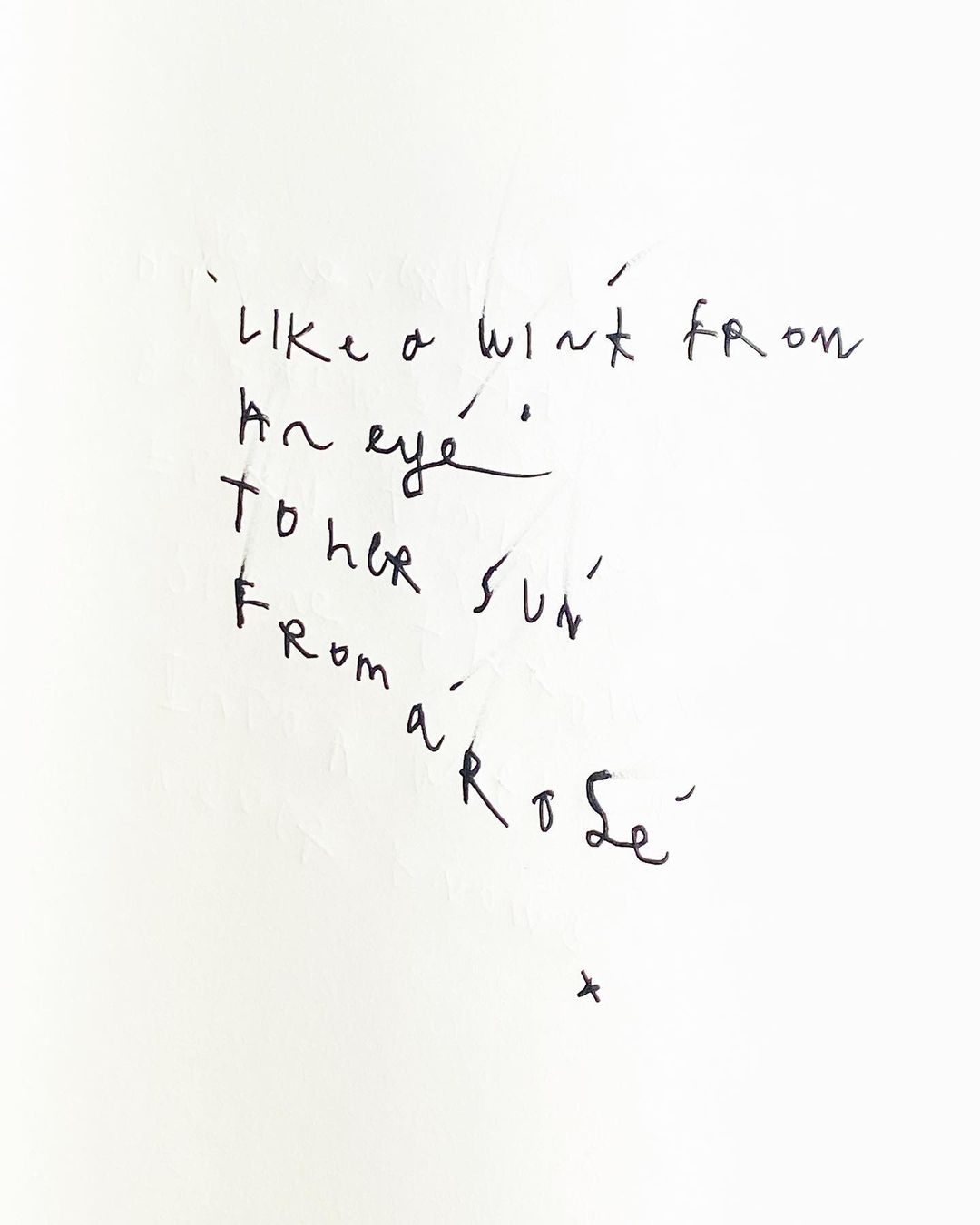Handwritten verse on white paper featuring cursive script in black ink. The text is centered and reads 'Like a wink from an eye'.