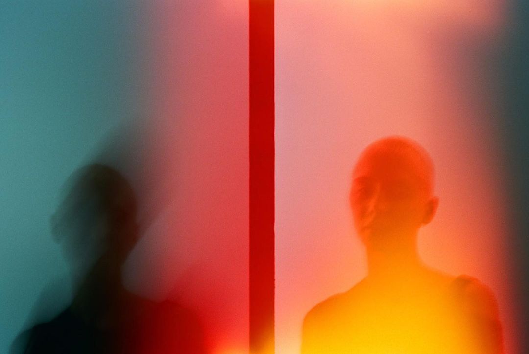Abstract portrait featuring a blurred person on the left with a person's glowing silhouette on the right, split by a red stripe.