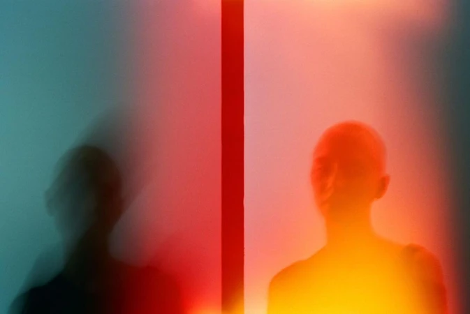Abstract portrait featuring a blurred person on the left with a person's glowing silhouette on the right, split by a red stripe.