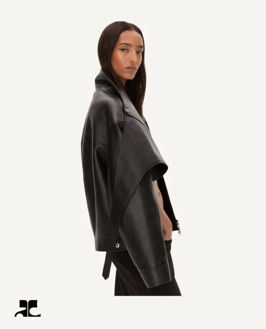 A brunette woman poses in a black leather jacket against a white backdrop, showcasing the jacket's design and style in a studio shot.