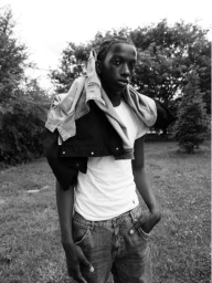 Black man wearing a white t-shirt and jeans with a jacket draped over his shoulder outdoors, photographed by Mark Elzey in London.