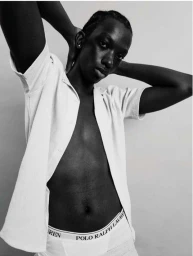 Black and white portrait of a man in a white unbuttoned short sleeve shirt and white briefs posing against a plain background.