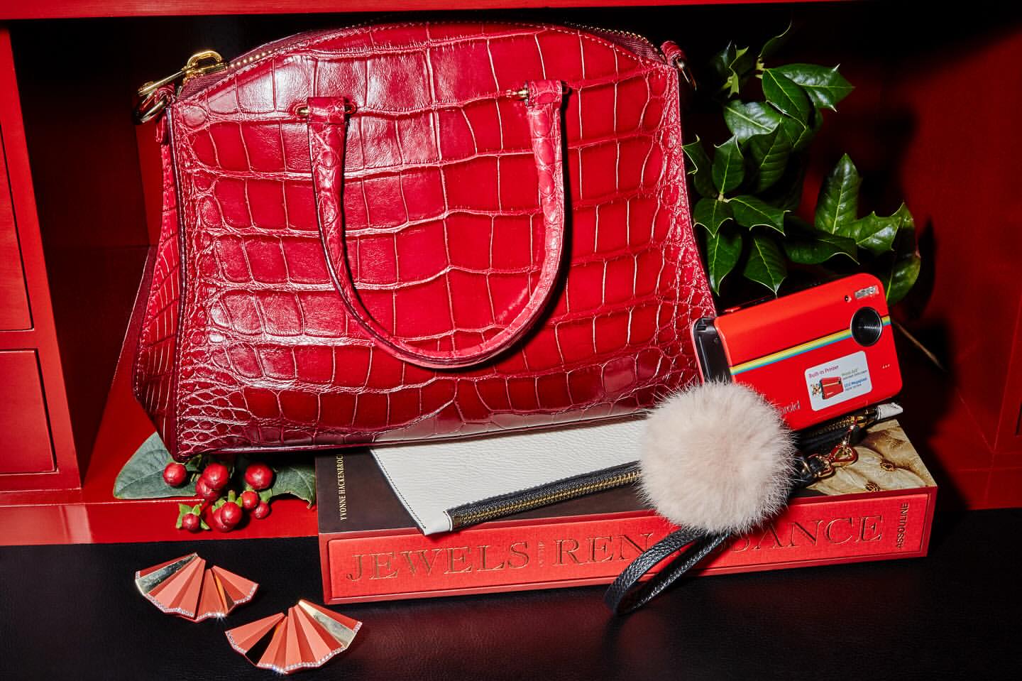 Red crocodile-leather purse with top handle, zipper closure, and gold hardware is displayed with a vintage camera and book.