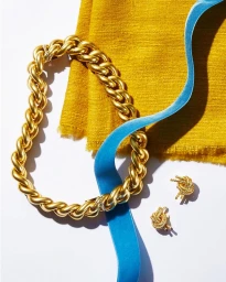 Thick gold chain necklace, matching earrings, yellow textured fabric and a blue ribbon on a white background.