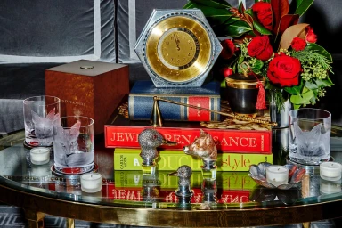 Decorative coffee table styled with books, an antique clock, crystal glassware with etched animal designs, and red roses