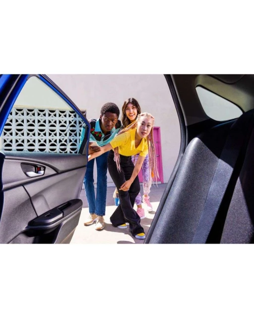Three young adults peek inside a blue car. Car door is open on a bright, sunny day. Two women and a man are smiling.