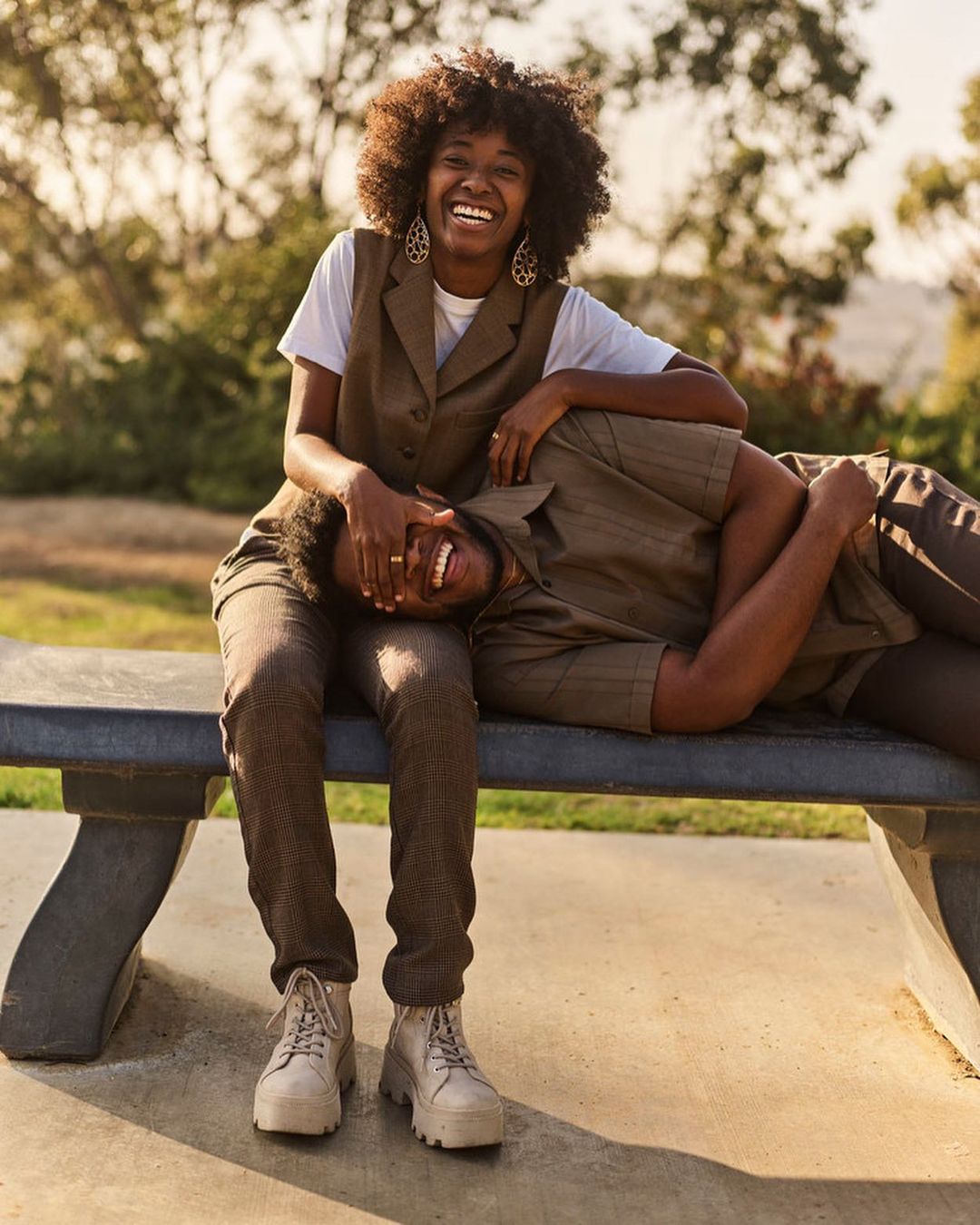 Outdoor shot of a smiling African-American woman sitting on a bench with a man laying with his head on her lap in a park.