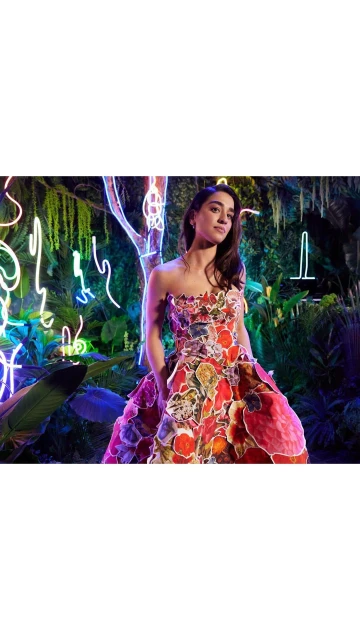 Adult female poses in a strapless floral gown in an indoor environment with neon lights and greenery. Fashion and beauty photography.