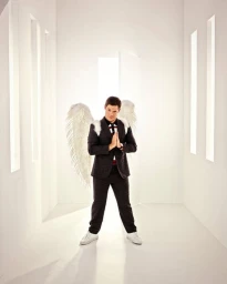 Man wearing a dark suit with white angel wings standing in a bright minimalist white corridor