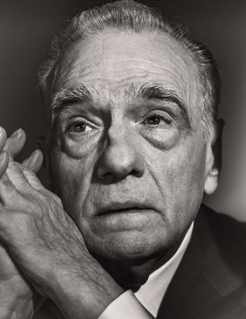 Monochrome portrait of a mature adult male with clasped hands, dressed in a suit with a white collared shirt in a photo studio setting.