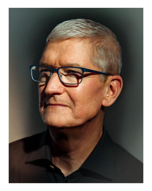 Portrait of an adult man with silver hair wearing glasses and a black shirt, shot in a photo studio with dark background lighting.