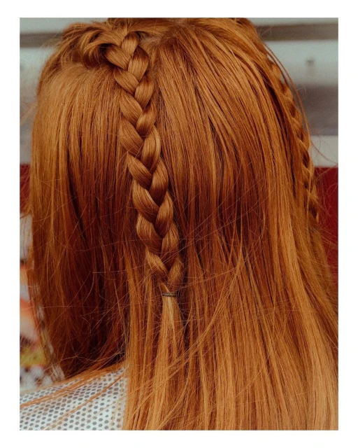 Close-up on copper-red long hair with a single braid along the hairline. Hair texture and color are the dominant visual elements.