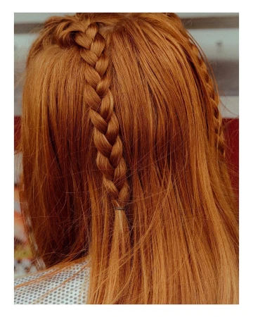Close-up on copper-red long hair with a single braid along the hairline. Hair texture and color are the dominant visual elements.