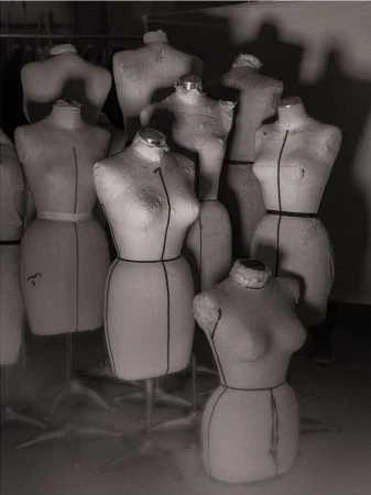 Monochrome photo of a group of dress forms on stands, arranged closely together in a studio setting. Soft lighting. 