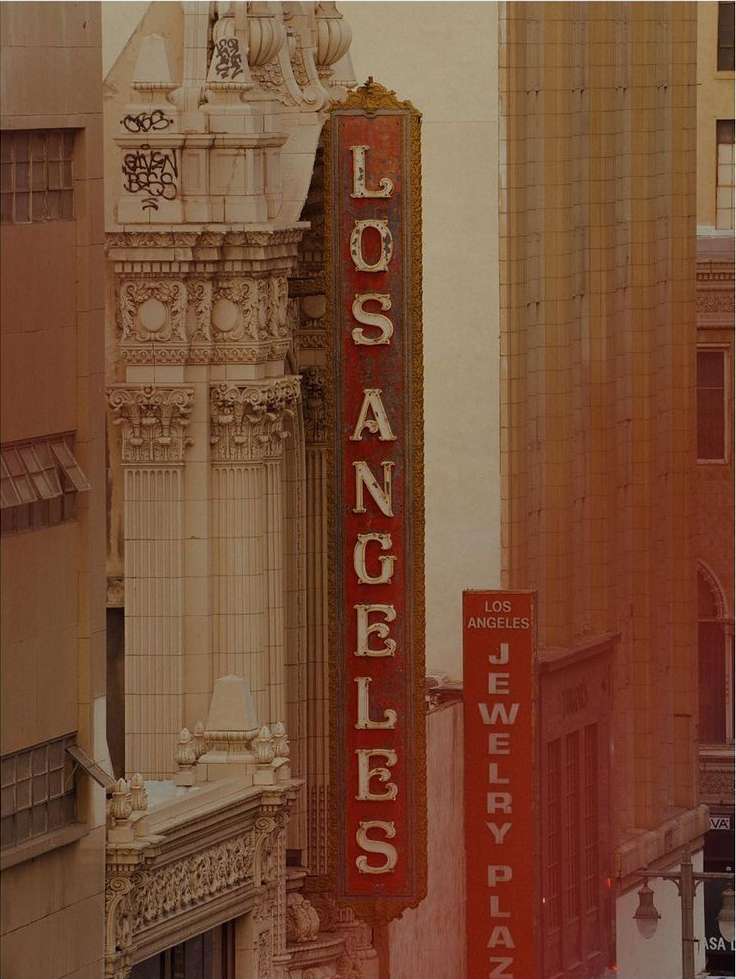 Vertical exterior photograph featuring a vintage red Los Angeles theater sign mounted on a historic architectural building