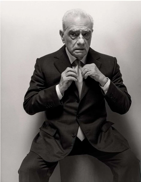 Portrait of an elderly man in a suit and tie, adjusting his tie, against a plain white backdrop, in a black and white photograph.