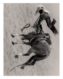 Black and white photograph of a rodeo cowboy bucking off a horse from a high overhead angle on a sandy arena floor