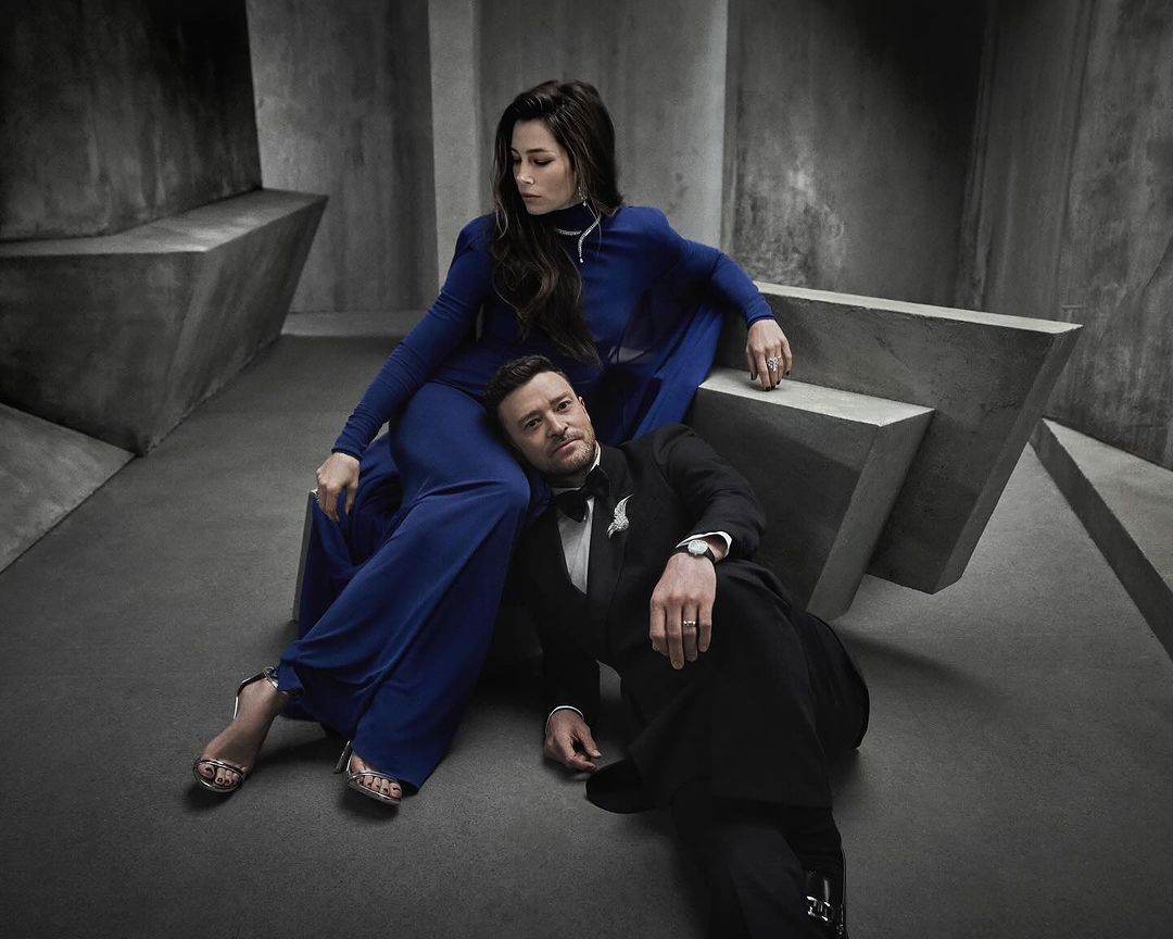 Justin Timberlake and Jessica Biel pose in a photo studio, with Timberlake seated on the floor and Biel sitting on a concrete structure.
