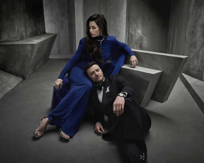 Justin Timberlake and Jessica Biel pose in a photo studio, with Timberlake seated on the floor and Biel sitting on a concrete structure.