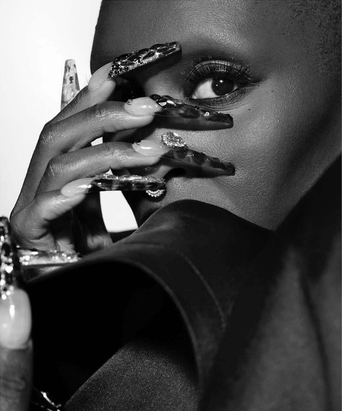 Close-up portrait of a Black woman holding elaborately embellished long fingernails near her face, photographed by Mark Seliger.