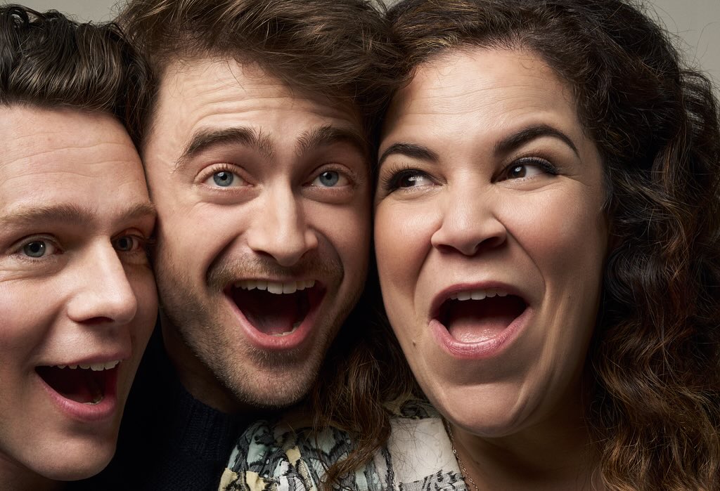 Three people—two men and one woman—posing closely together and smiling broadly with open mouths in a well-lit photo studio shot.