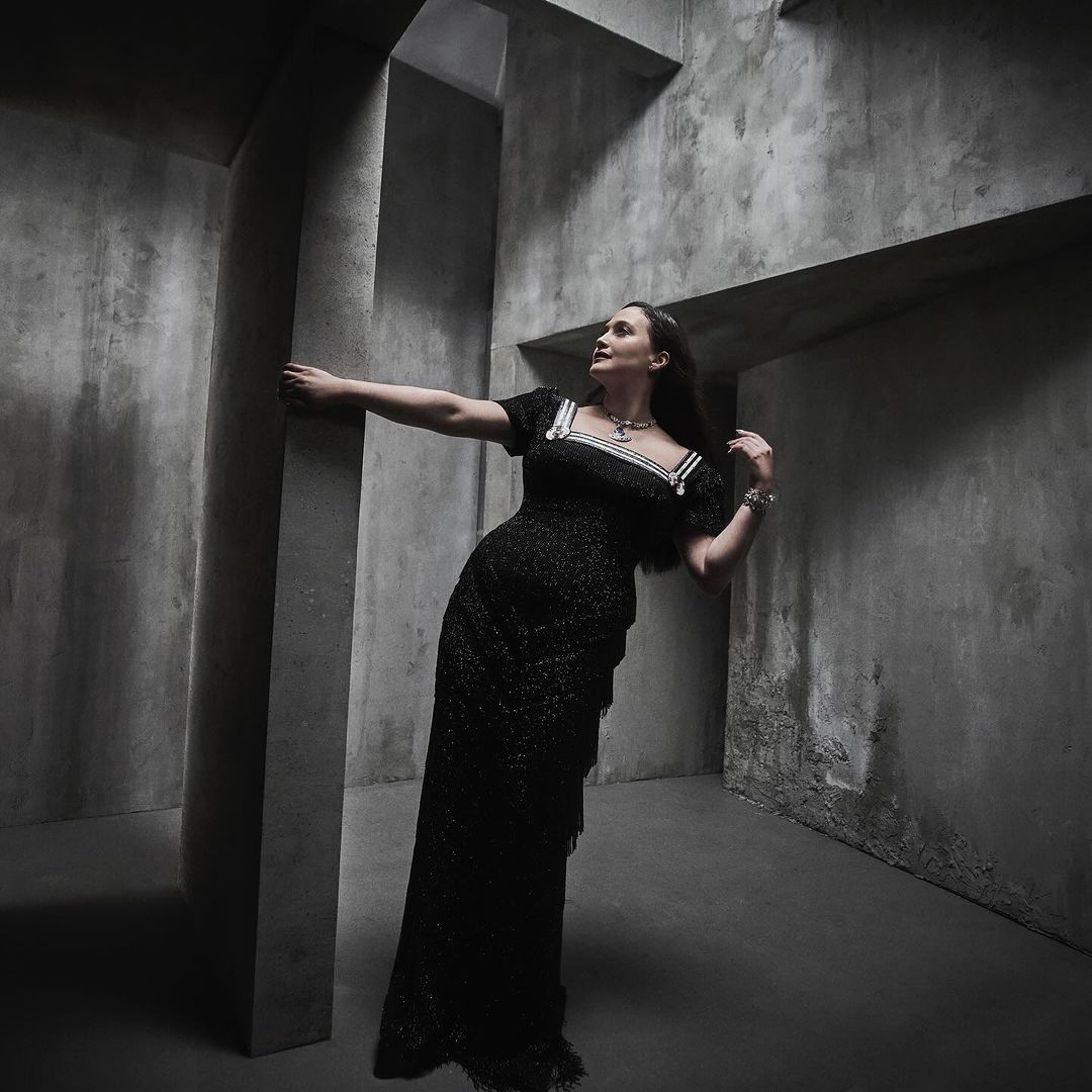 Woman in dark sparkly dress posing inside a concrete architectural interior with textured walls
