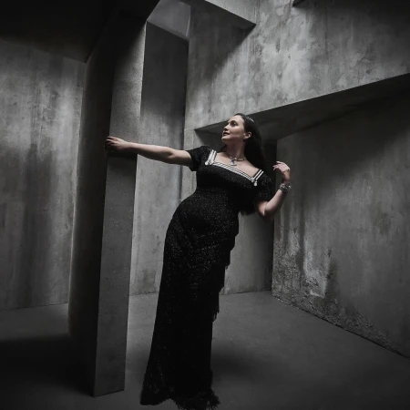 Woman in dark sparkly dress posing inside a concrete architectural interior with textured walls