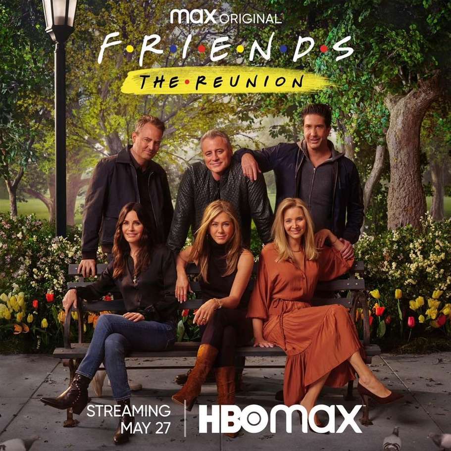 The cast of Friends sitting together on a bench in front of trees and greenery for The Reunion, streaming May 27 on HBO Max.