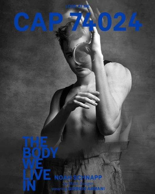 Black and white portrait of a shirtless male model holding a round object in front of his face. Magazine cover. Blue text overlay.