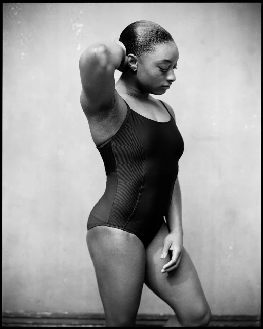 Monochrome portrait of an African American woman in a swimsuit, hand behind her head, gazing downward in a photo studio setting.