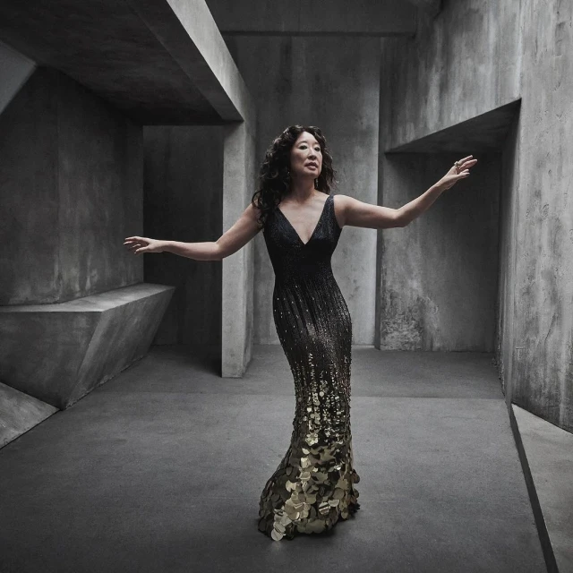 Sandra Oh strikes an elegant pose in a black and gold sequined gown against a geometric, concrete backdrop, adding a touch of sophistication.