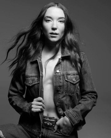 Portrait of a woman wearing an open denim jacket against a neutral studio background, captured in monochrome by Mark Seliger.