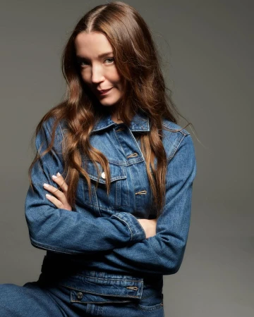 Woman in denim jacket with arms crossed posing against a grey seamless studio background