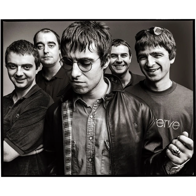 Black and white portrait of the band Oasis, featuring five members in a close-up studio shot, showcasing their individual styles and expressions.
