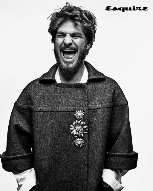 Black and white portrait of a man with curly hair, open mouth, and wearing a coat with brooches on a light background.