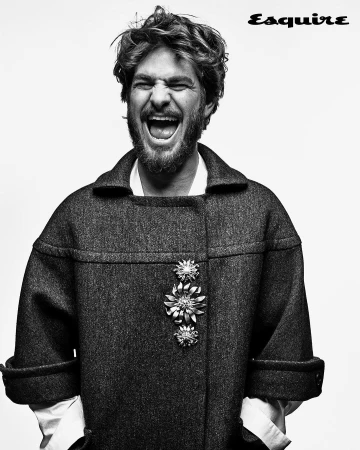 Black and white portrait of a man with curly hair, open mouth, and wearing a coat with brooches on a light background.