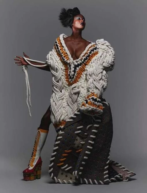 Fashion editorial shot of a stylish adult woman wearing an avant-garde outfit with textured fabrics and platform shoes in a studio.