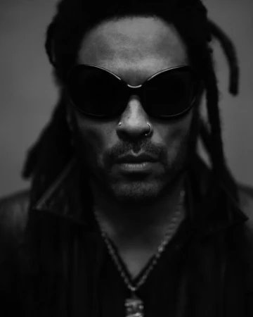 Portrait of an adult male with locs and sunglasses in a monochromatic photo studio shot, wearing a leather jacket and silver necklace.