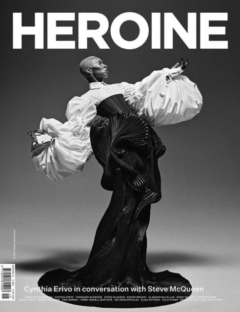 Heroine magazine cover featuring Cynthia Erivo wearing a white blouse and black textured dress, posing against a grey backdrop.
