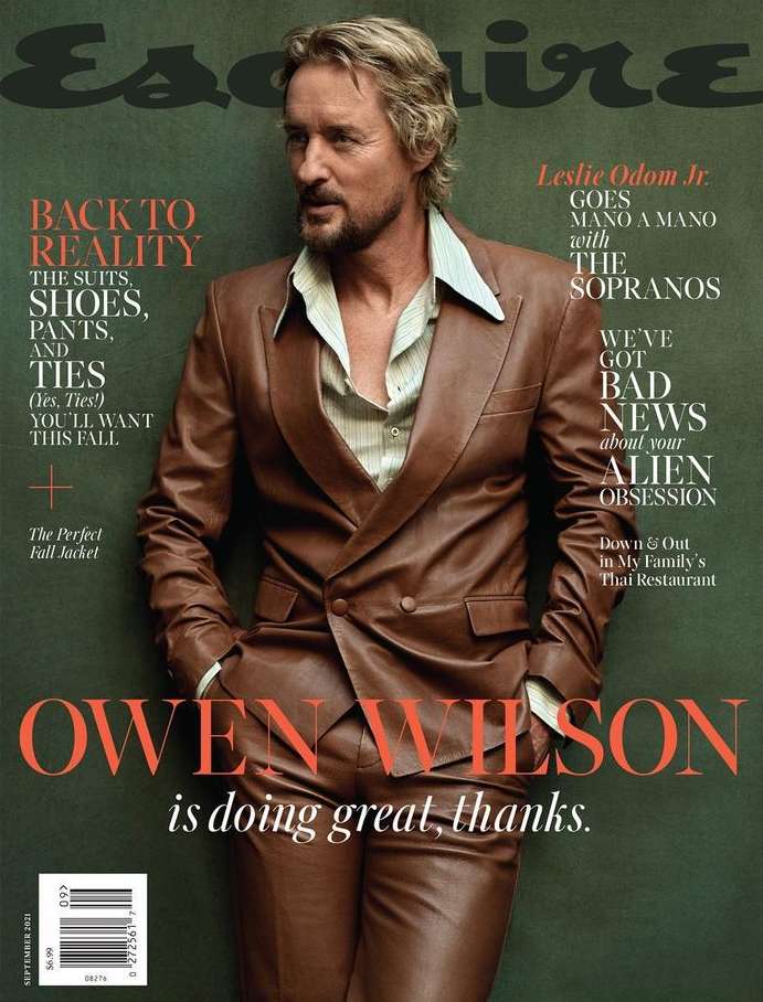 Magazine cover featuring Owen Wilson in a brown leather suit, posing against a muted green background, with the magazine's title.