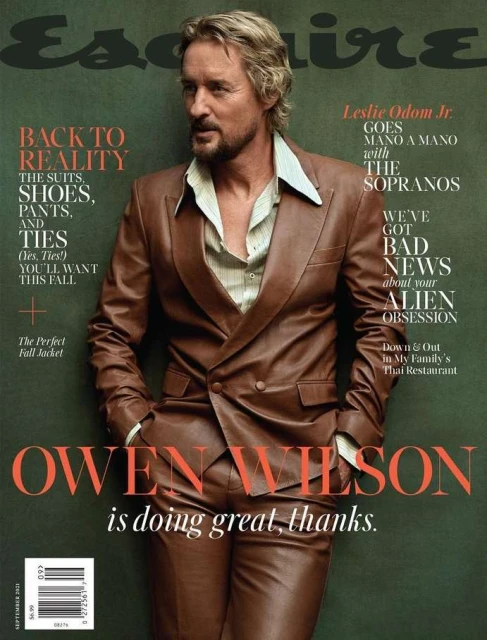 Magazine cover featuring Owen Wilson in a brown leather suit, posing against a muted green background, with the magazine's title.