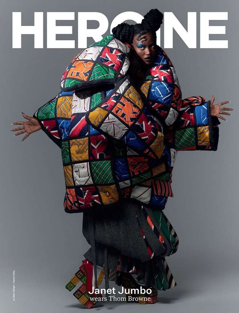 Heroine magazine cover featuring Janet Jumbo wearing an oversized colorful quilted coat with graphic patterns, styled hair, and makeup.