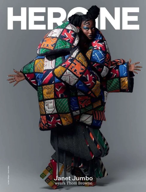 Heroine magazine cover featuring Janet Jumbo wearing an oversized colorful quilted coat with graphic patterns, styled hair, and makeup.